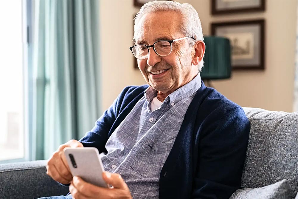 A male senior using his mobile phone inside an assisted living home for seniors