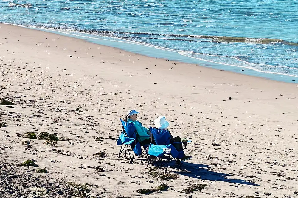 Two elderly women sit chair at the beach talking and watching the sun and the sea near assisted living home for seniors